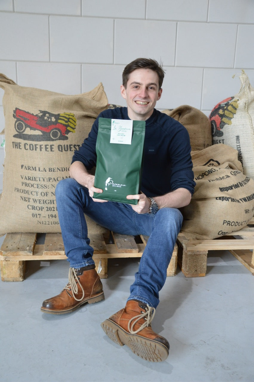 Vincent voor balen koffie met zak koffiebonen van Pacamara in zijn handen